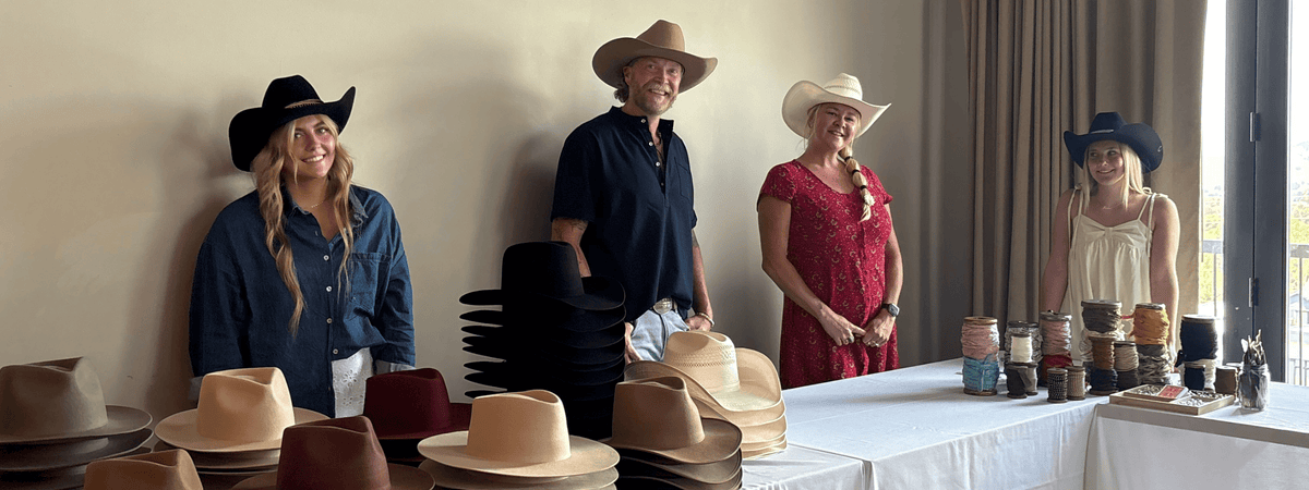 People behind a table full of several hats and hat accessories at a custom hat bar event.