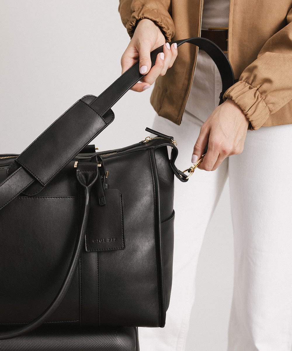 Person holding a black vegan leather weekender bag against a plain background #color_black