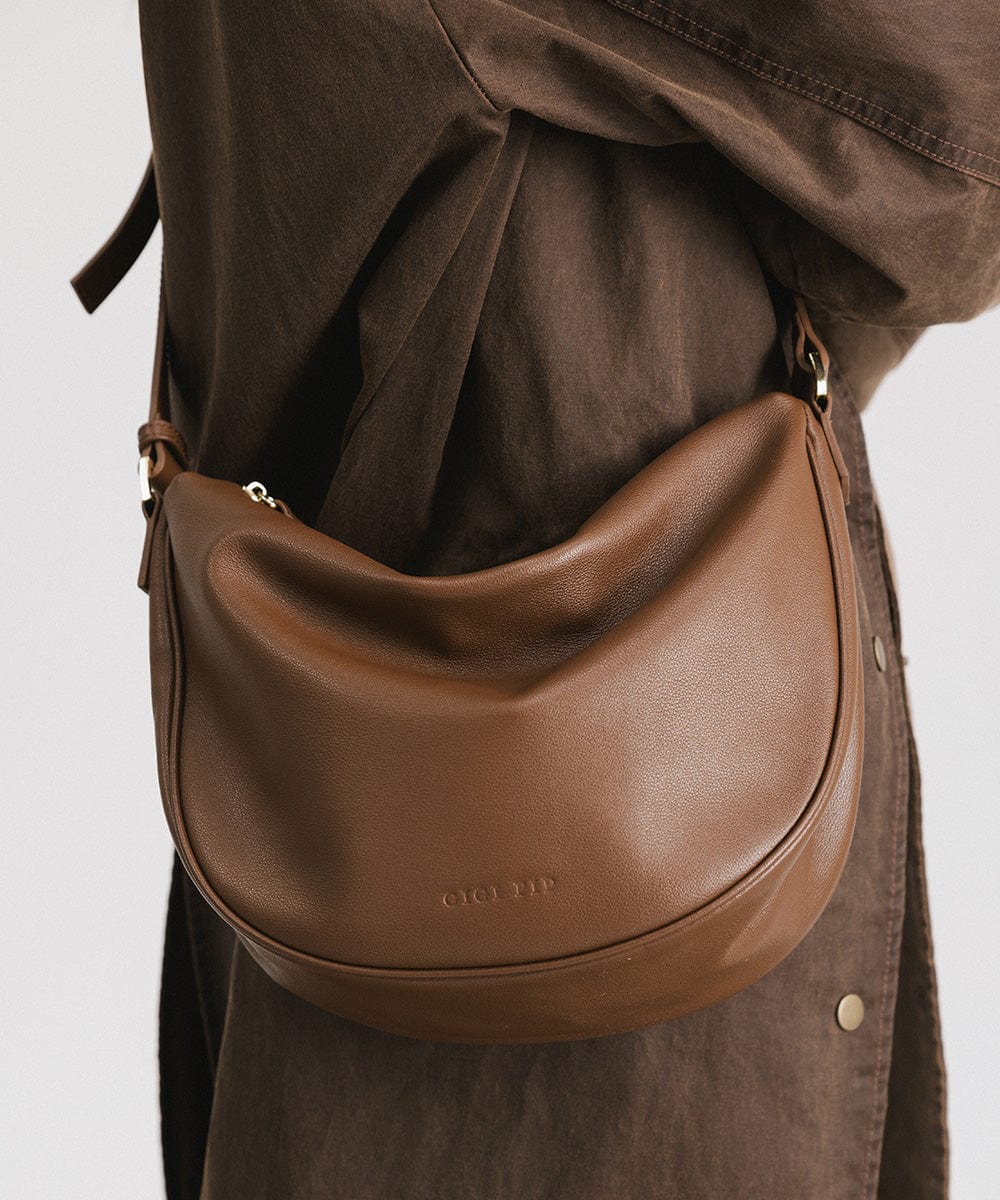 A chocolate colored genuine leather slouchy bag with a shoulder strap and zipper closure carried by someone wearing a brown shirt against a plain background #color_chocolate