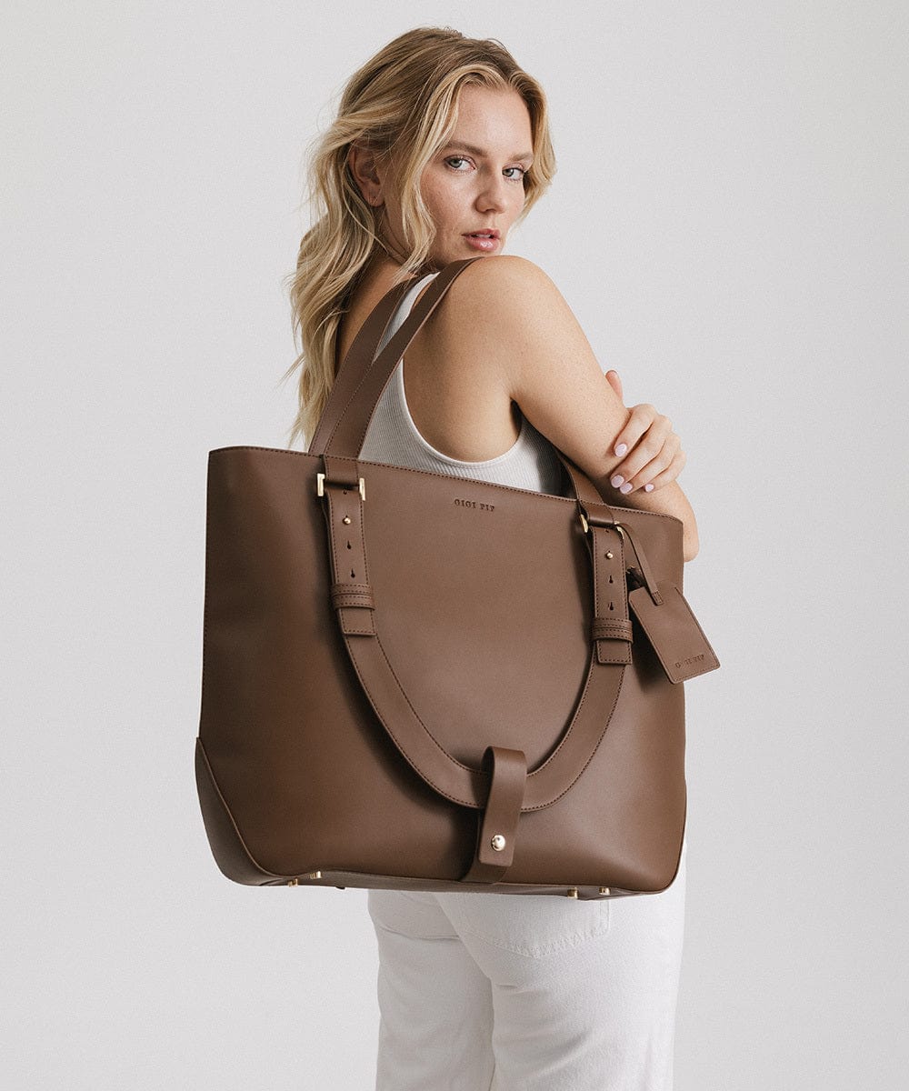 Woman carrying a brown Hayes Hat Carrying Tote Bag against a plain background #color_chocolate