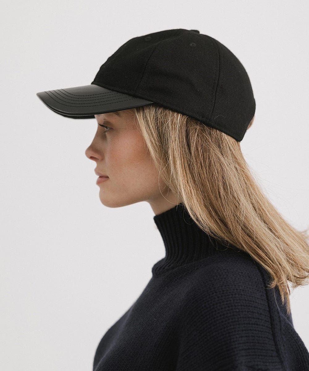 Woman wearing a black cap and a black sweater, facing sideways against a plain background #color_black