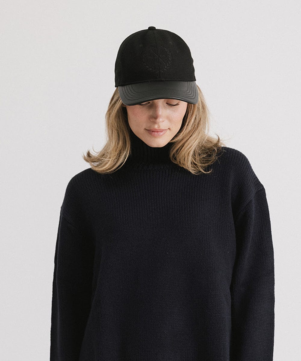 Woman wearing a black cap with a logo and a black sweater against a plain background #color_black