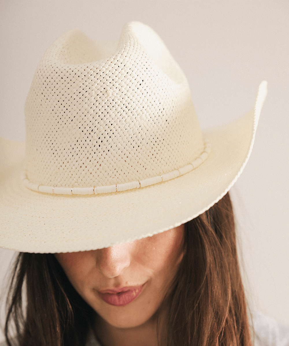 Woman wearing a beige straw hat with a decorative band in a white background #color_cream