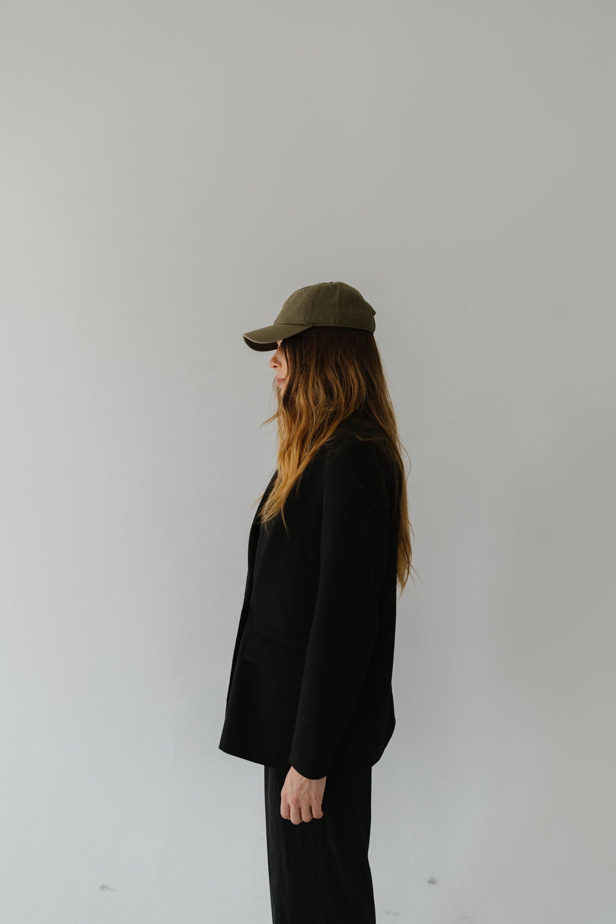 Woman wearing an olive colored ball cap, a black shirt and black pants, facing sideways against a plain background #color_olive