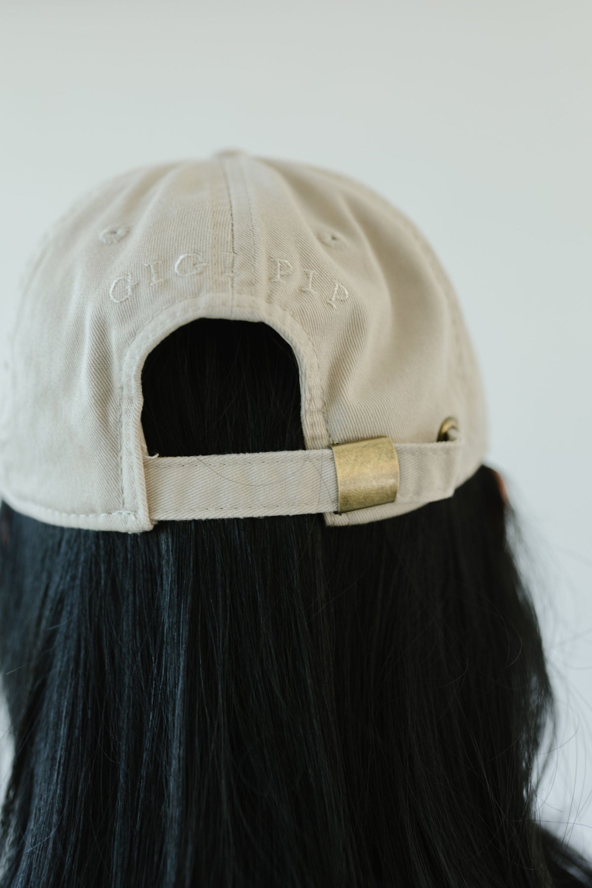 Woman wearing a cream colored ball cap facing behind against a plain background #color_cream