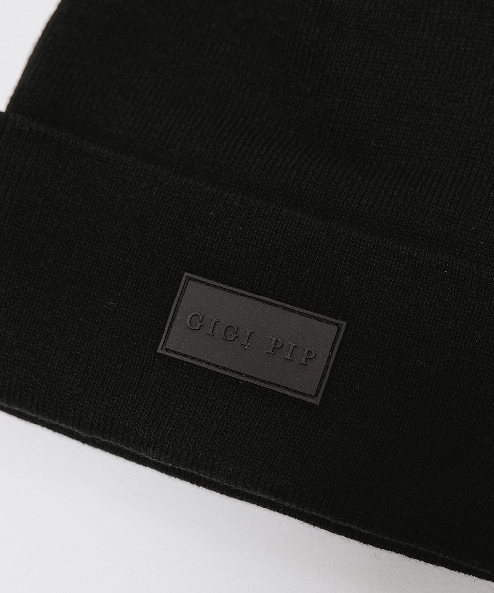 Close up image of a black knit beanie with the brand label on a white background #color_black
