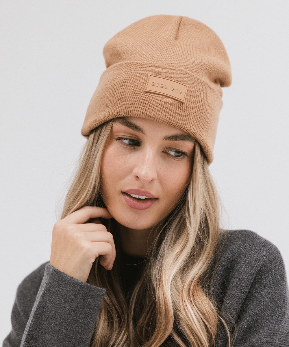 Woman wearing a latte colored knit beanie and a grey sweater against a plain background #color_latte