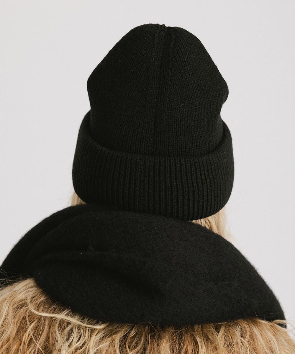 Person wearing a black oversized knit beanie and a black scarf against a plain background #color_black