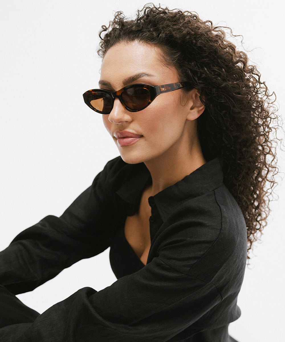 Woman wearing tortoise colored cat eye sunglasses and a black shirt against a white background #color_tortoise