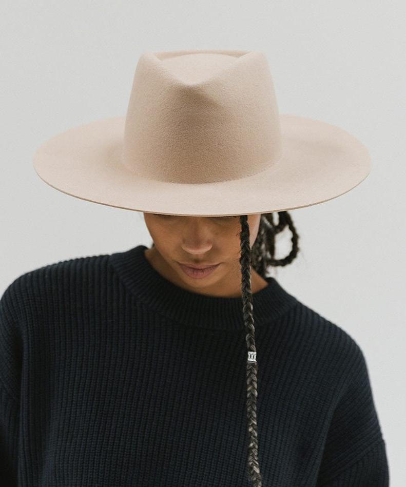 Woman wearing a cream wide brim felt hat with a triangle crown and a dark blue sweatshirt against a white background #color_cream