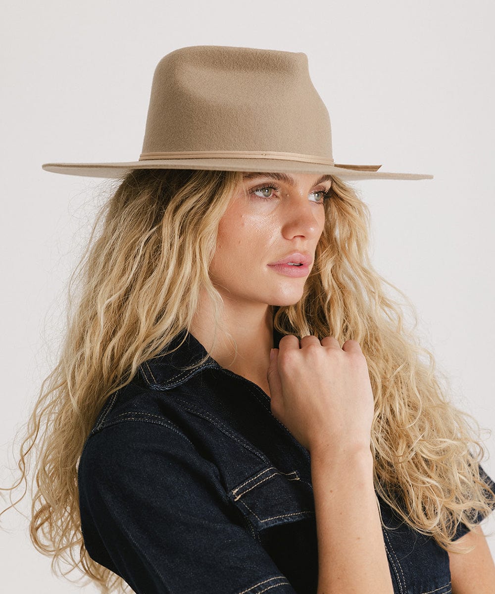 Woman with long blonde hair wearing a tan fedora hat and a denim shirt, looking sideways against a plain background #color_tan