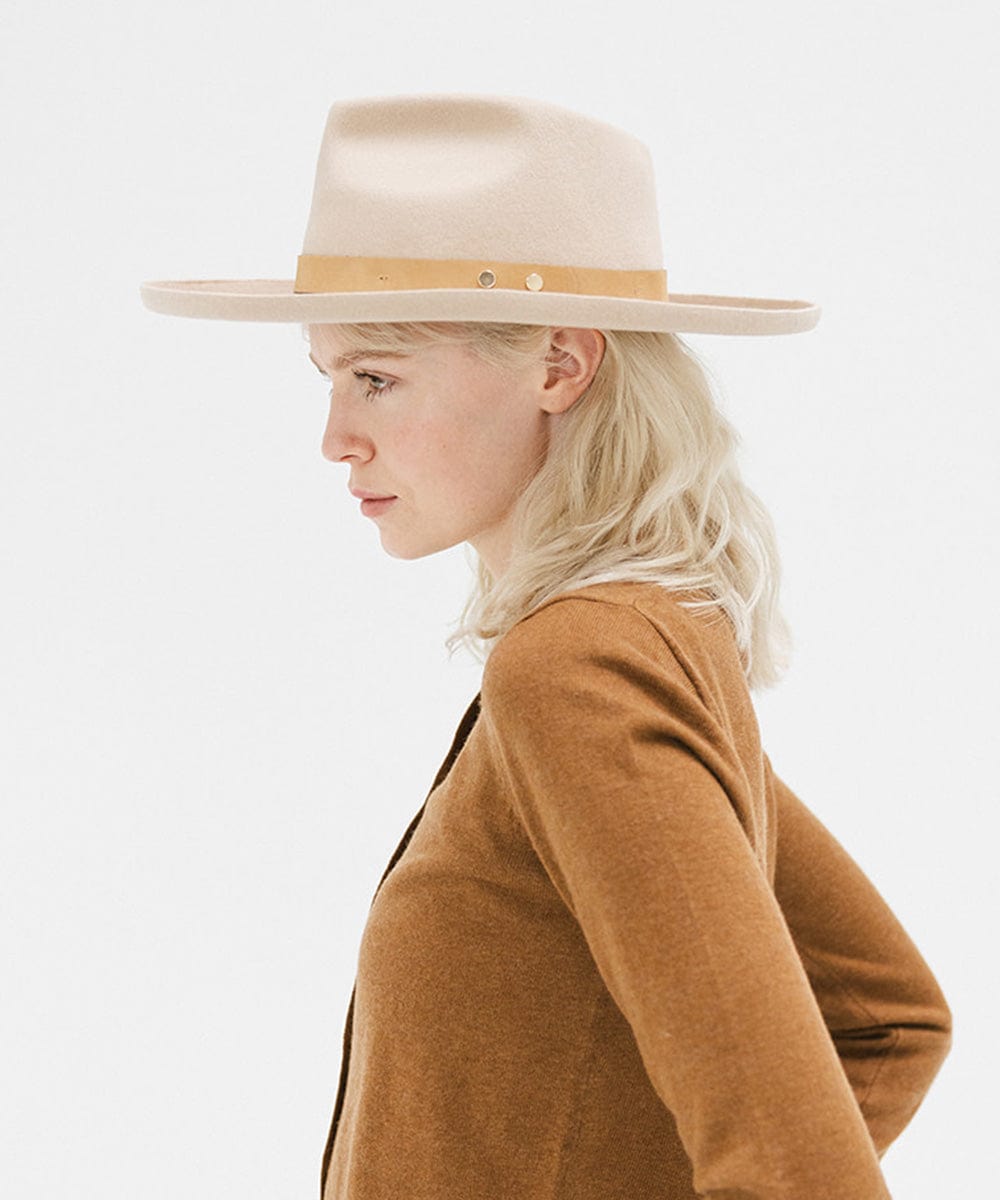 Woman wearing a cream felt fedora hat with a hat band and a brown sweater, looking sideways against a plain background #color_cream