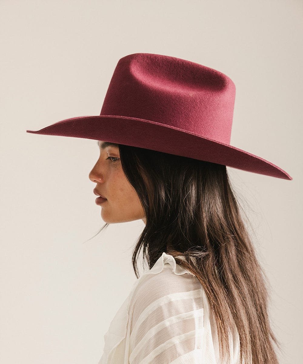 Woman wearing a merlot colored cowboy hat and a white shirt, facing sideways against a plain background #color_merlot