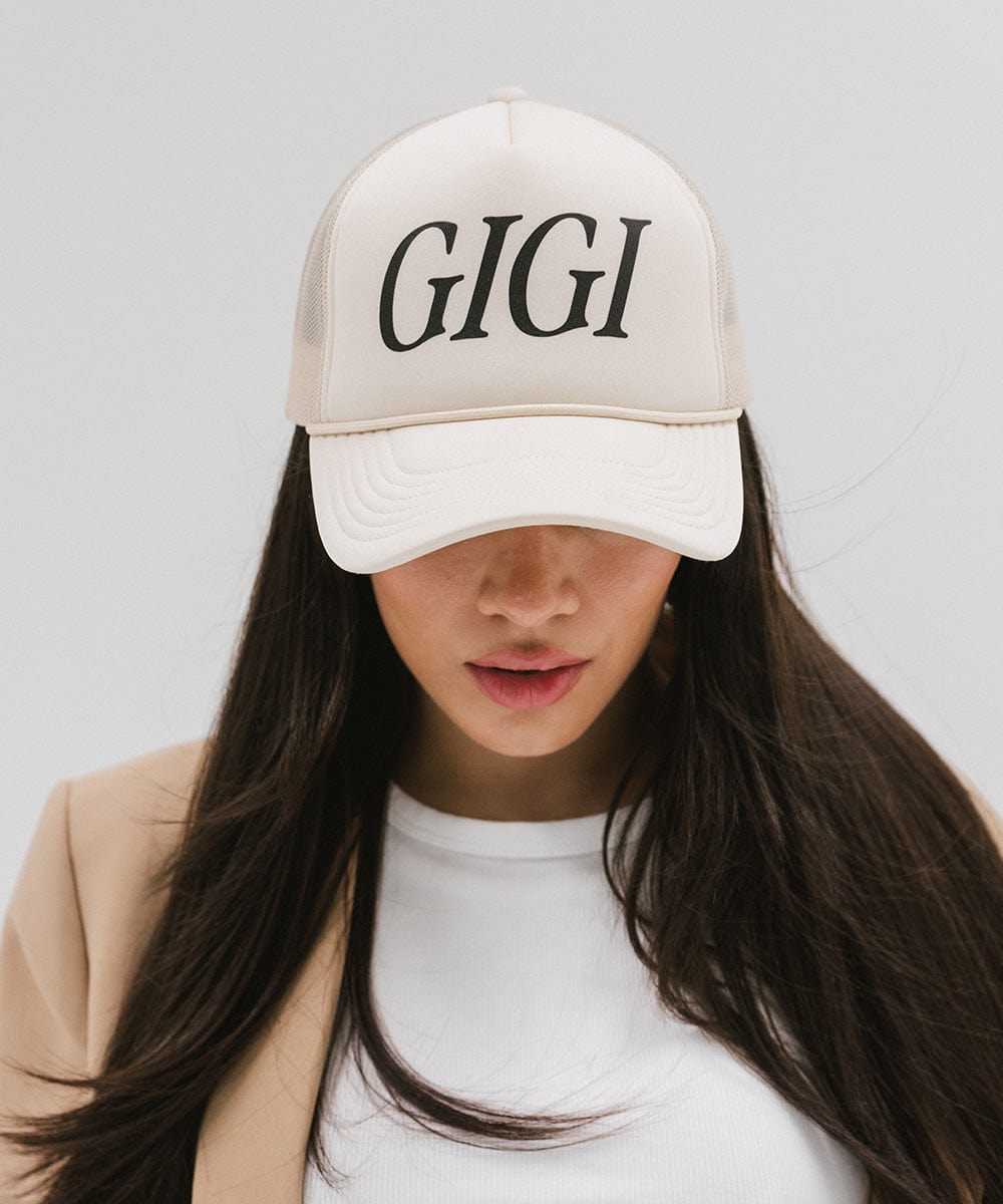 Woman wearing a cream cap with 'GIGI' text and a white top against a plain background #color_cream