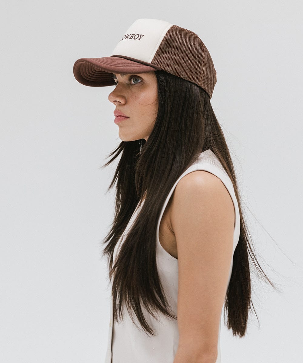 Woman wearing a cream and chocolate brown cap and a white top, facing sideways against a plain background #color_cream - chocolate brown