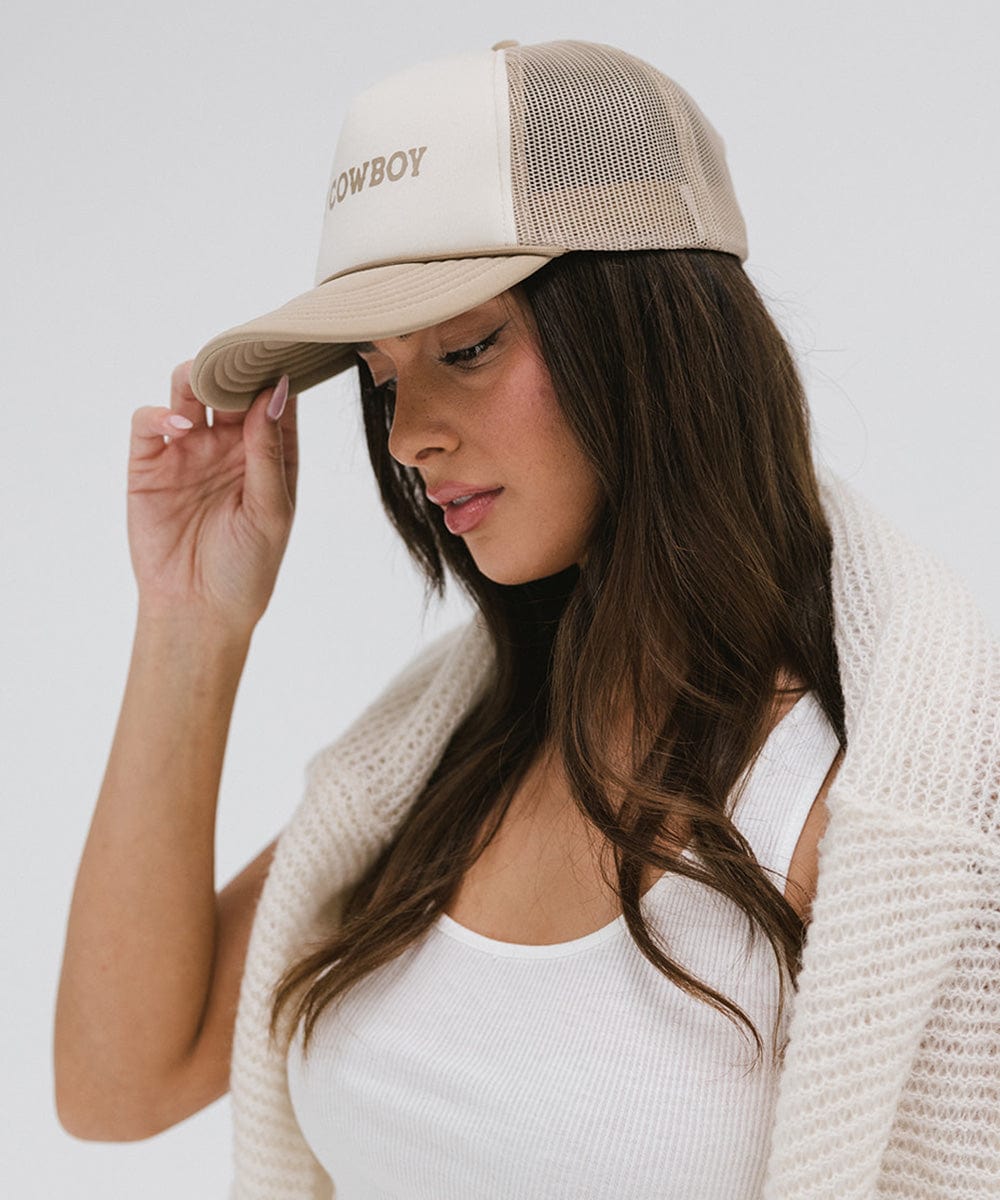 Woman wearing a tan and cream cap with 'Hey Cowboy' text and a white top, posing sideways against a plain background #color_cream - tan