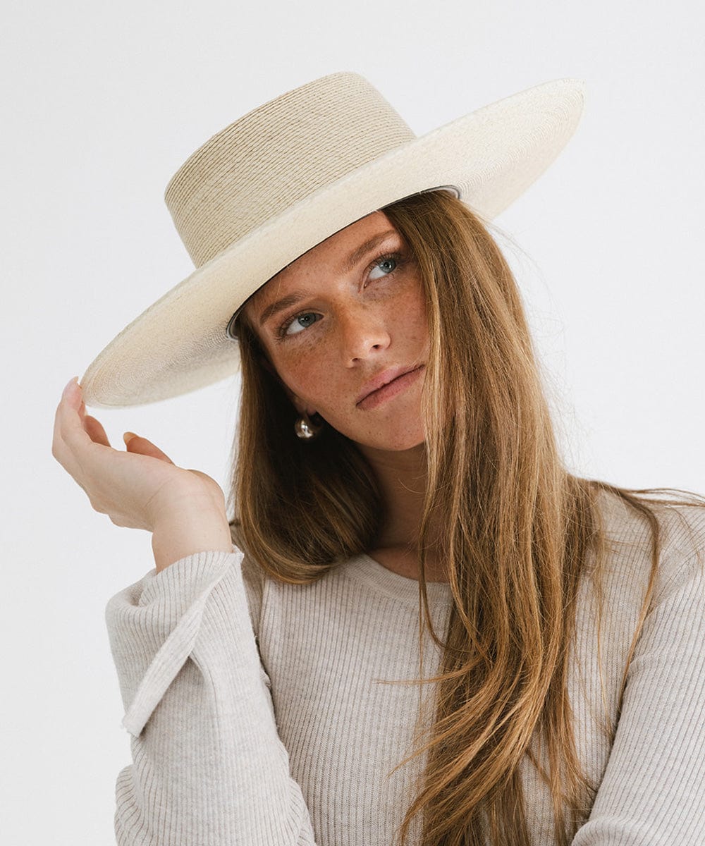 Woman wearing a natural colored straw boater hat and a white top against a plain background #color_natural