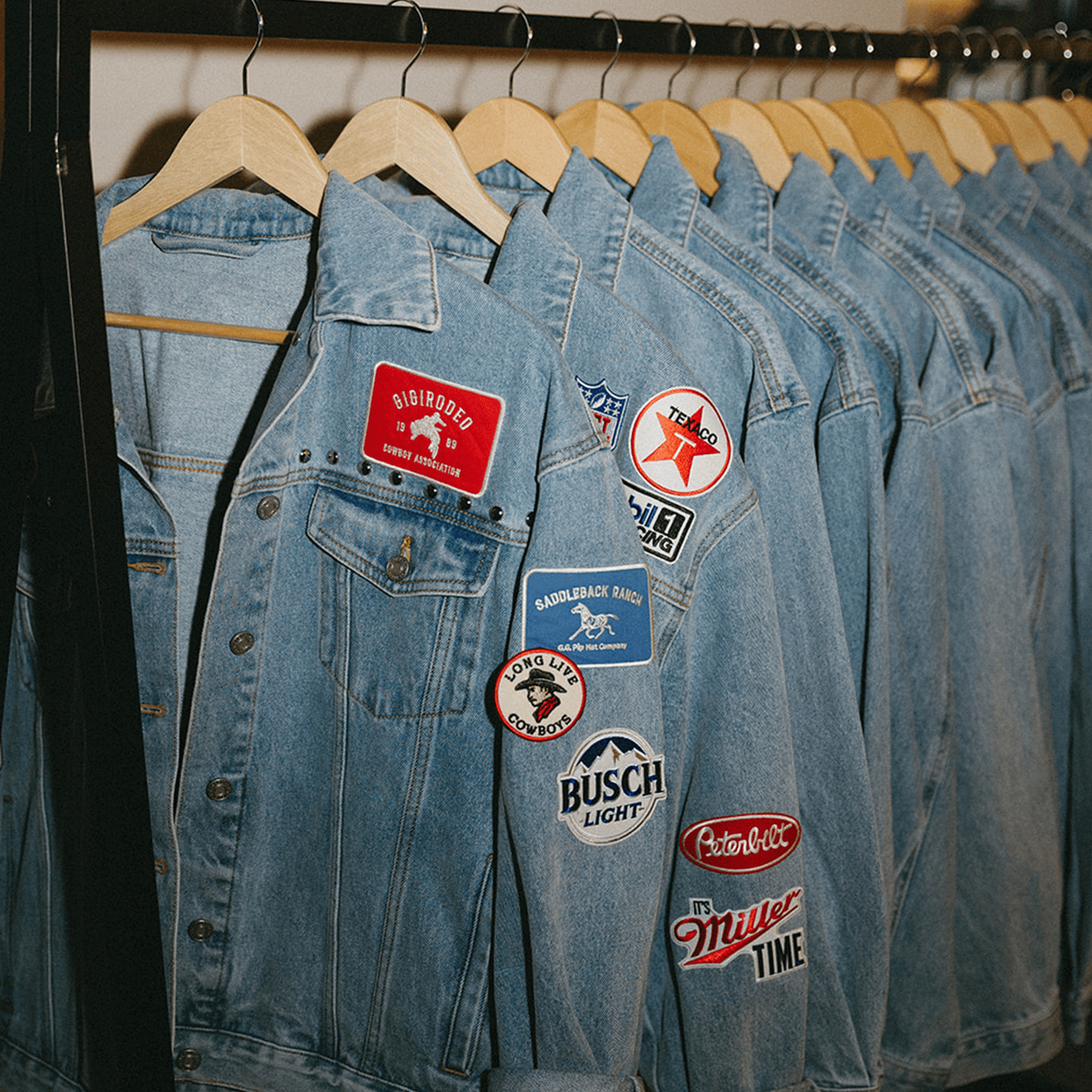 Row of denim jackets with various patches on a rack at a custom hat bar event.