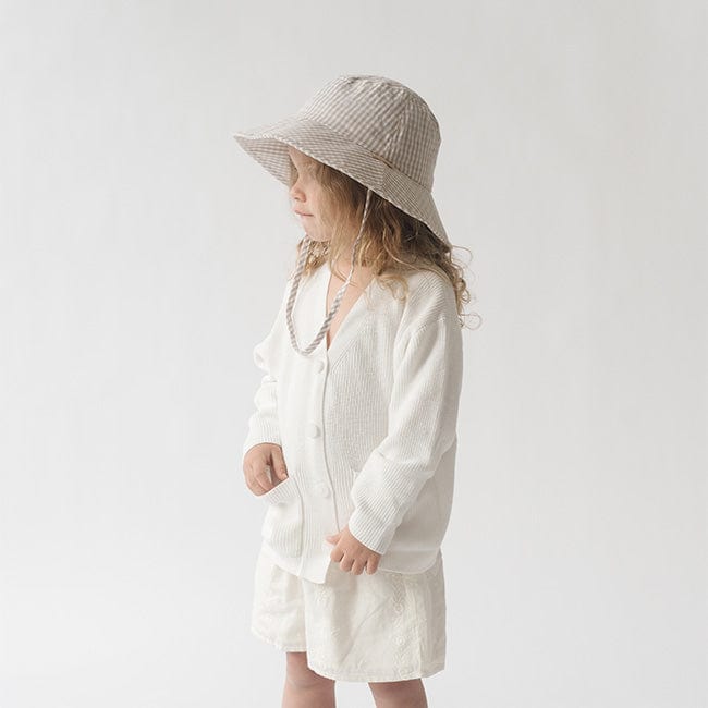 Young girl wearing a latte colored bucket hat, a white shirt and white shorts, posing sideways against a plain background #color_latte