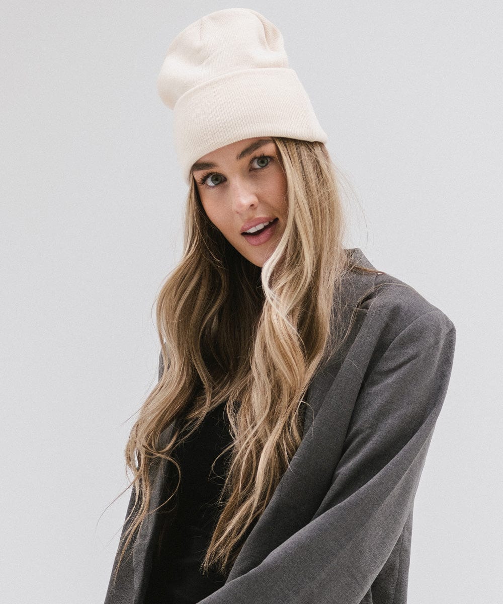 Woman wearing a cream beanie and a grey coat, posing against a plain background #color_cream