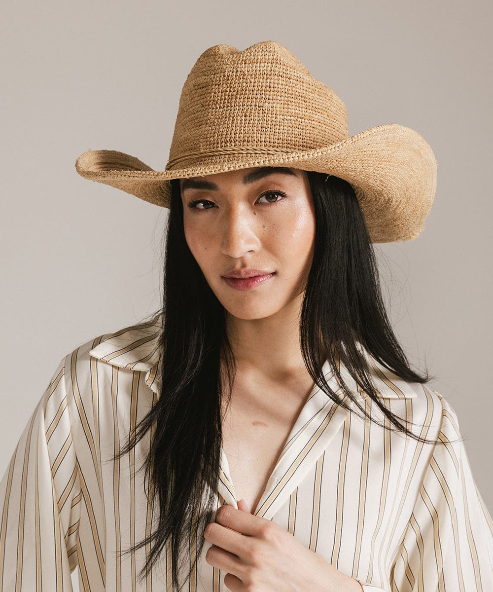 Woman wearing a natural colored straw cowboy hat and a light colored shirt against a plain background #color_natural