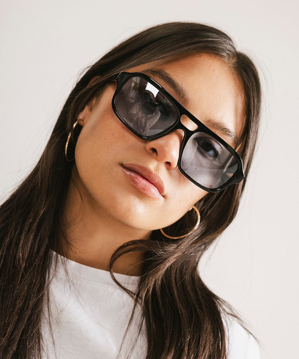 Woman wearing black sunglasses and a white t-shirt against a plain background #color_black