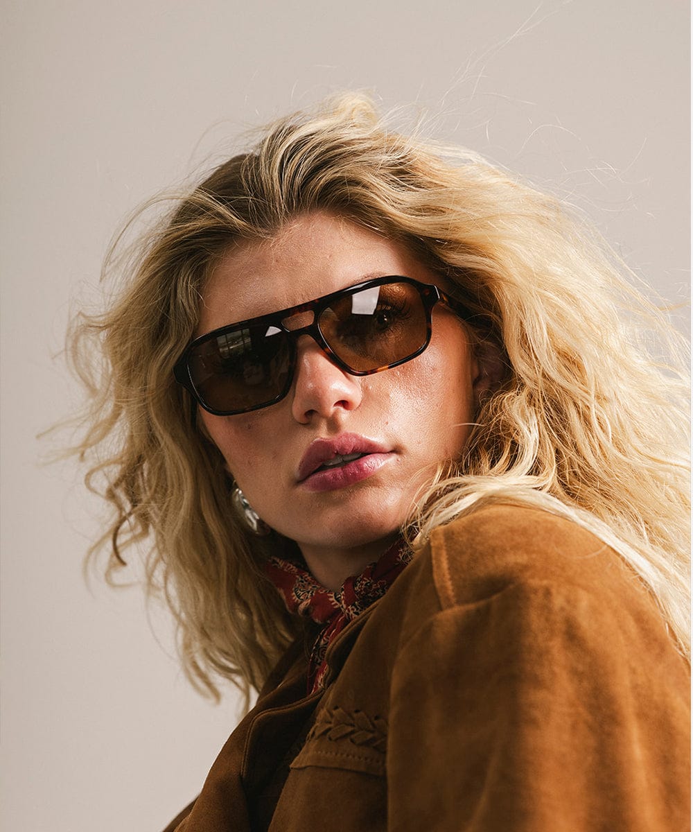 Person wearing sunglasses and a brown jacket with a neutral background #color_tortoise