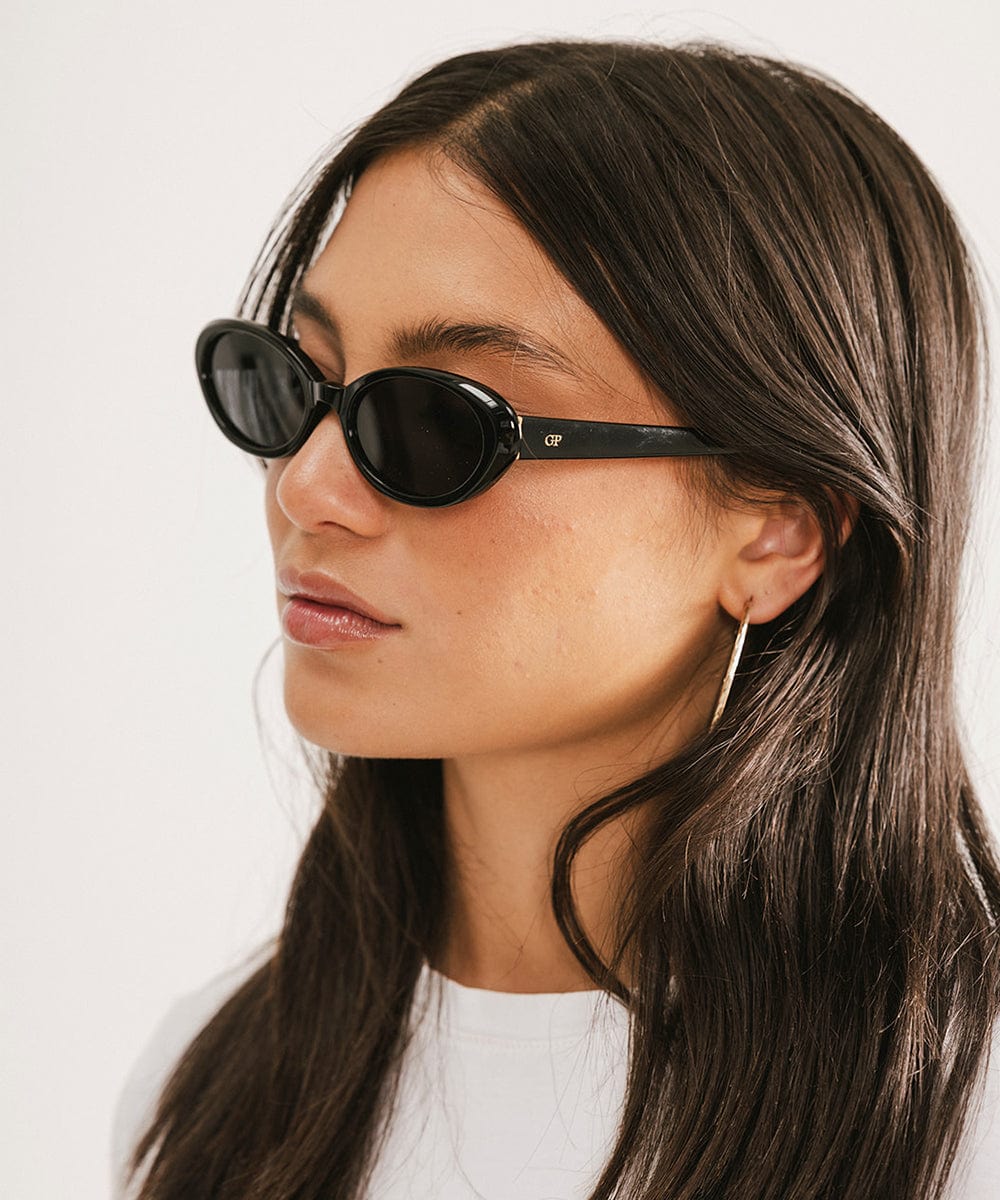 Woman wearing black sunglasses facing sideways against a plain background #color_black