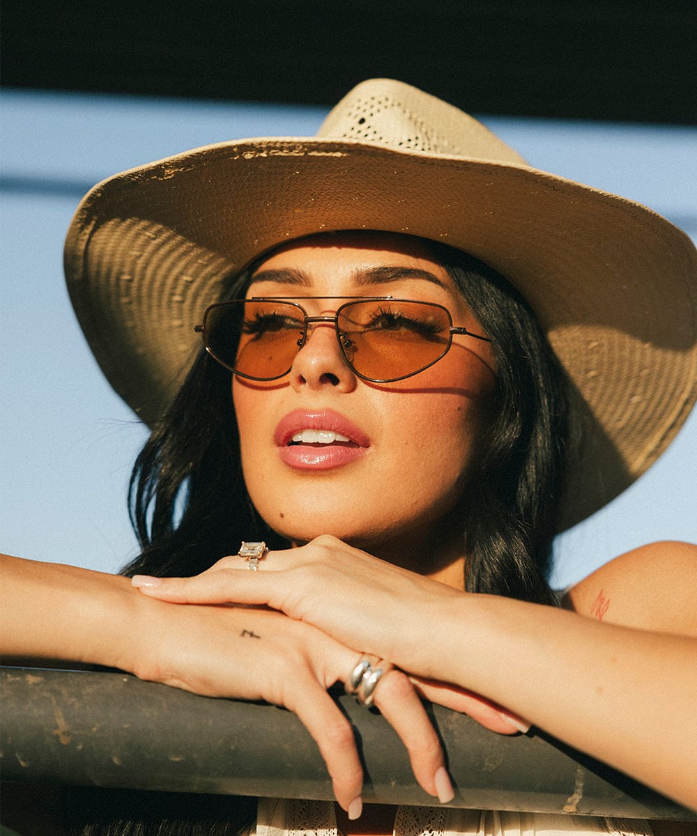 Woman wearing a straw hat and brown sunglasses against a blue background #color_brown