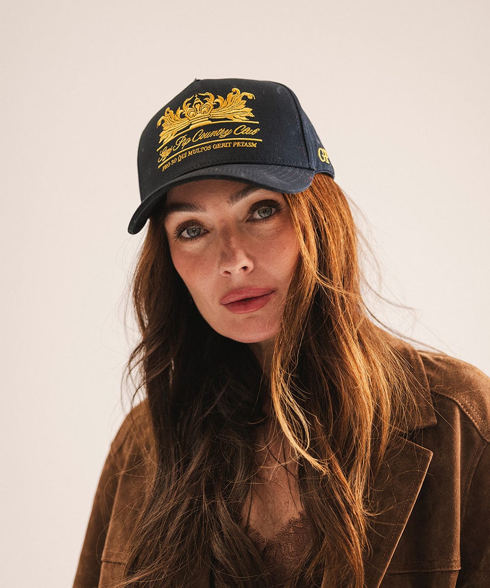 Woman wearing a black cap with gold text and a brown jacket on a light background #color_navy