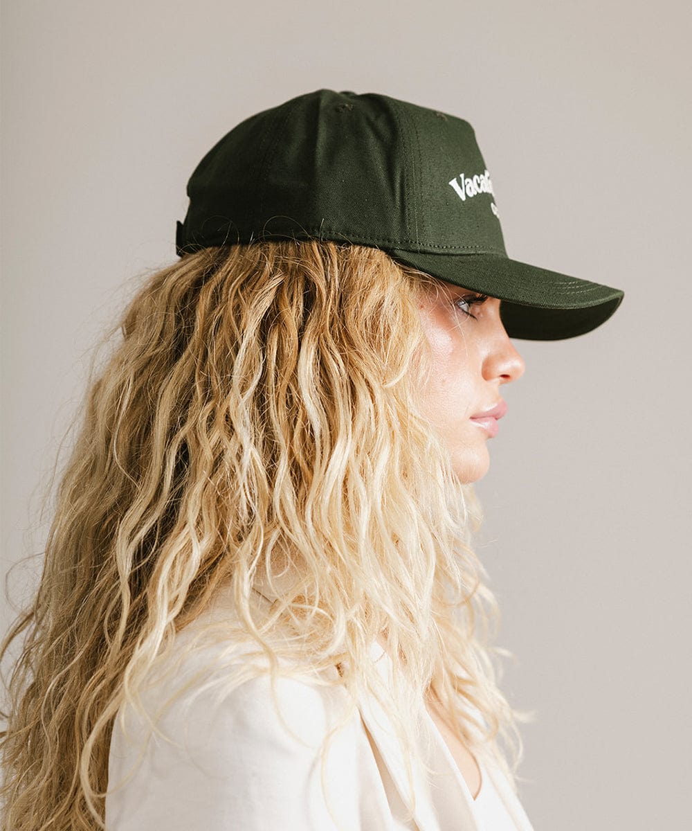 Woman wearing a dark green cap and a white coat, facing sideways against a plain background #color_dark green