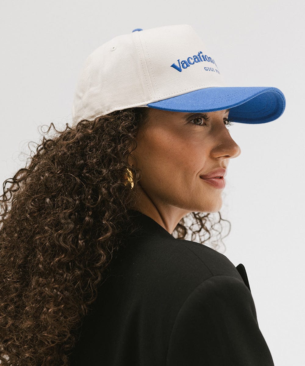 Woman wearing a cream and blue cap with 'Vacation Club' text and a black blazer, facing sideways against a plain background #color_cream - blue