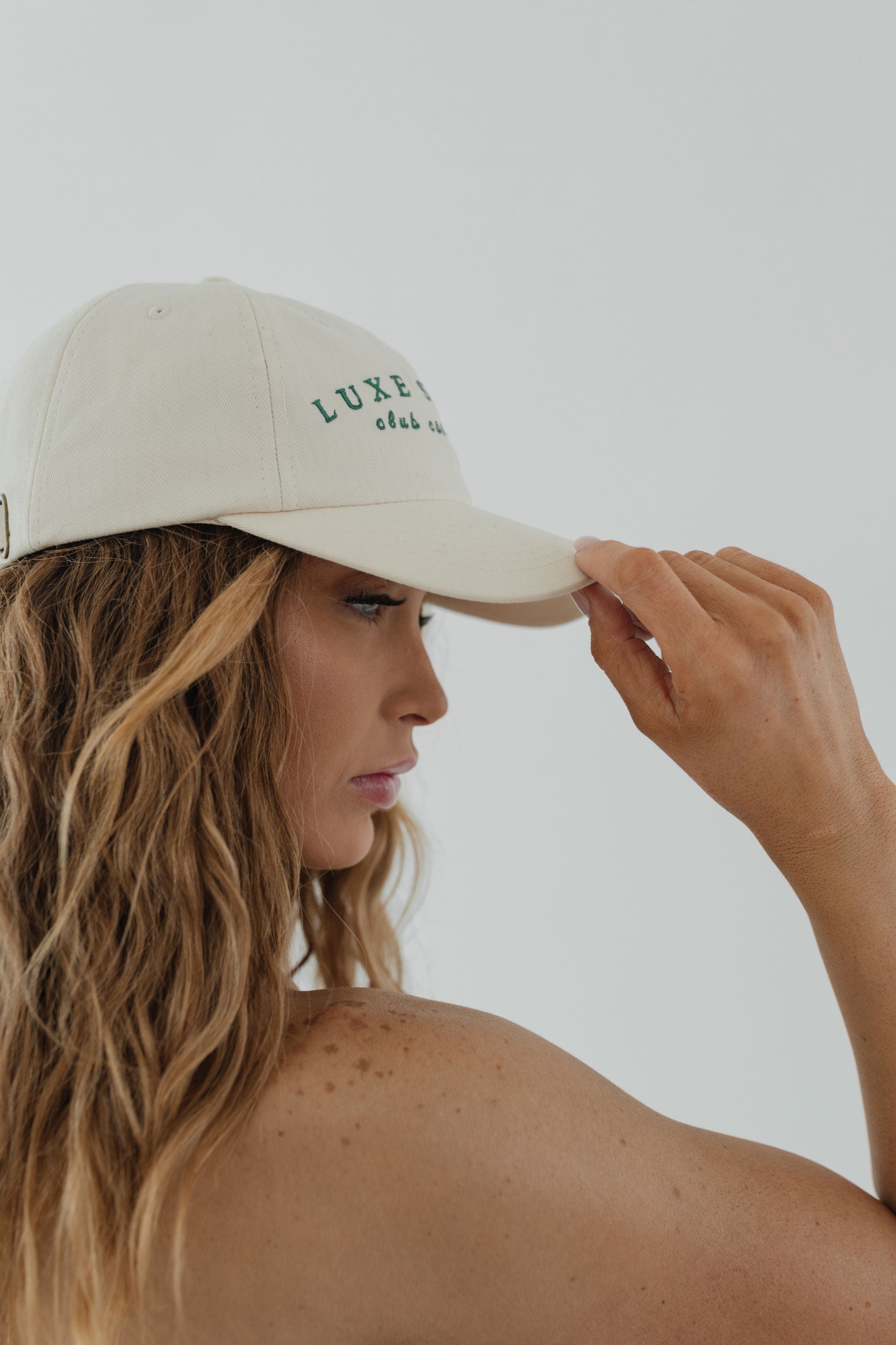 Woman wearing a cream ball cap facing sideways against a plain background #color_cream