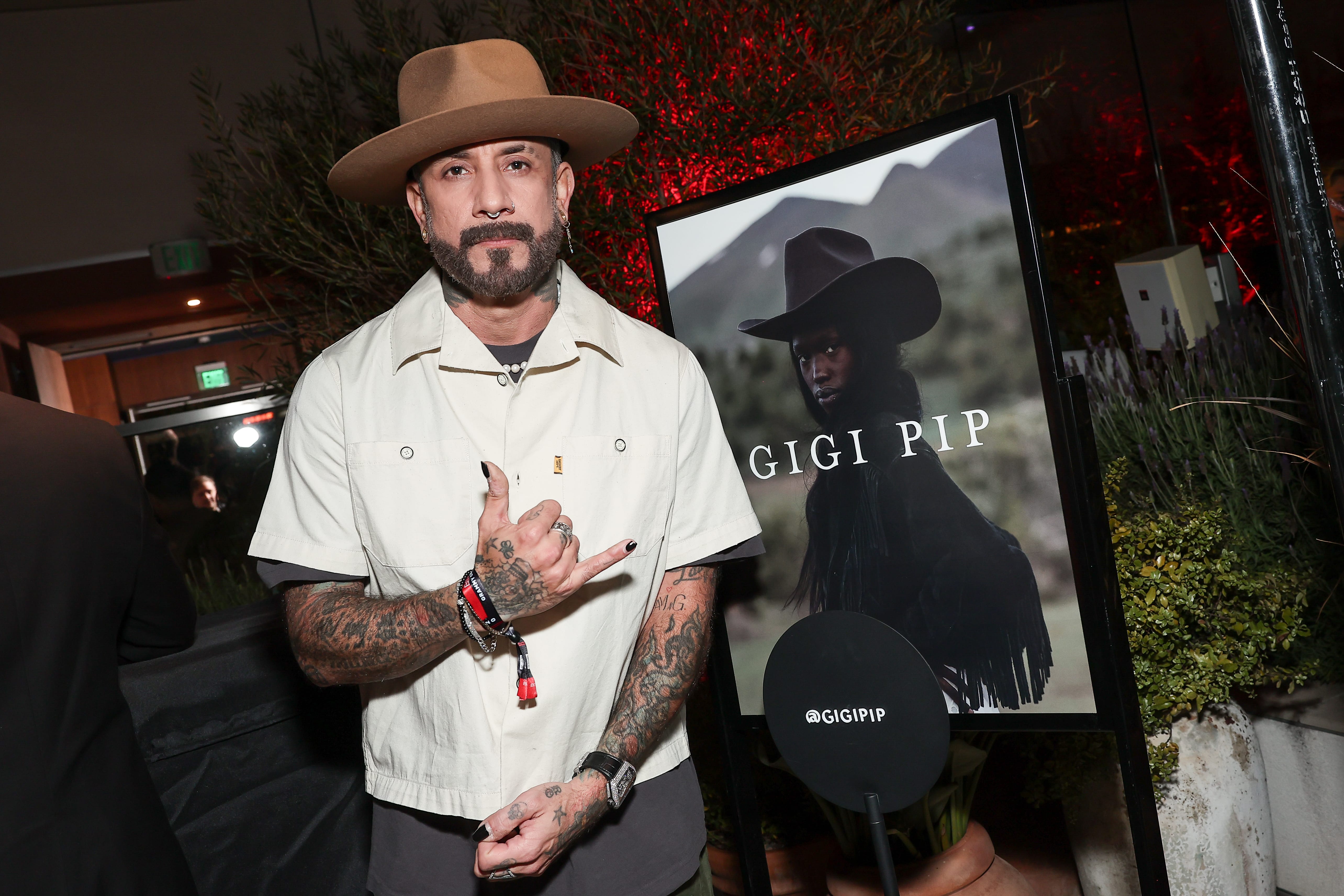 Man in a white shirt and brown hat posing beside a signage displaying 'GIGI PIP' at a custom hat bar event.