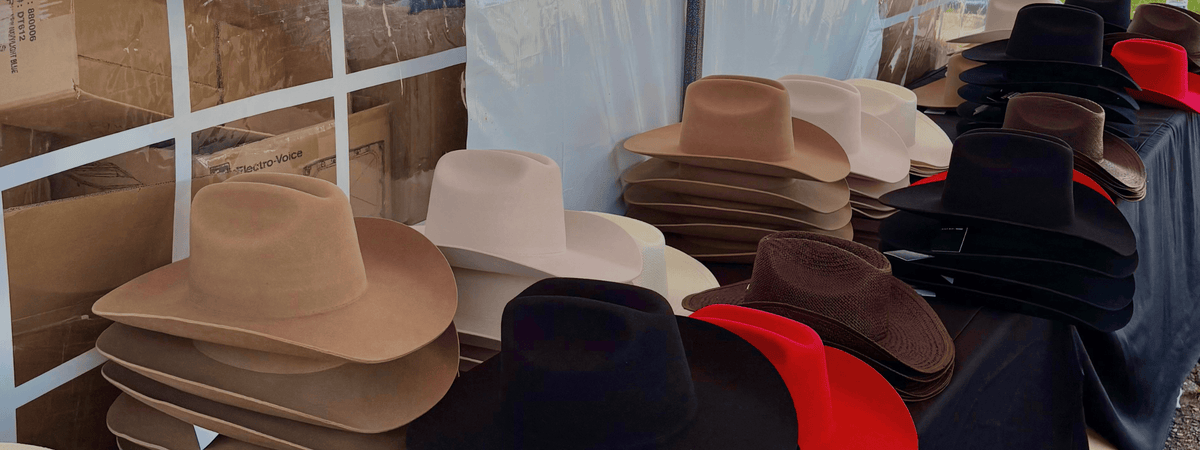 A display of various cowboy-style felt hats in multiple colors, including beige, brown, black, white, and red, arranged on a table at a custom hat bar event.
