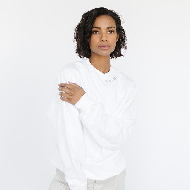 Woman wearing a white sweatshirt with the text 'GIGI PIP' in beige  against a plain background #color_white-beige