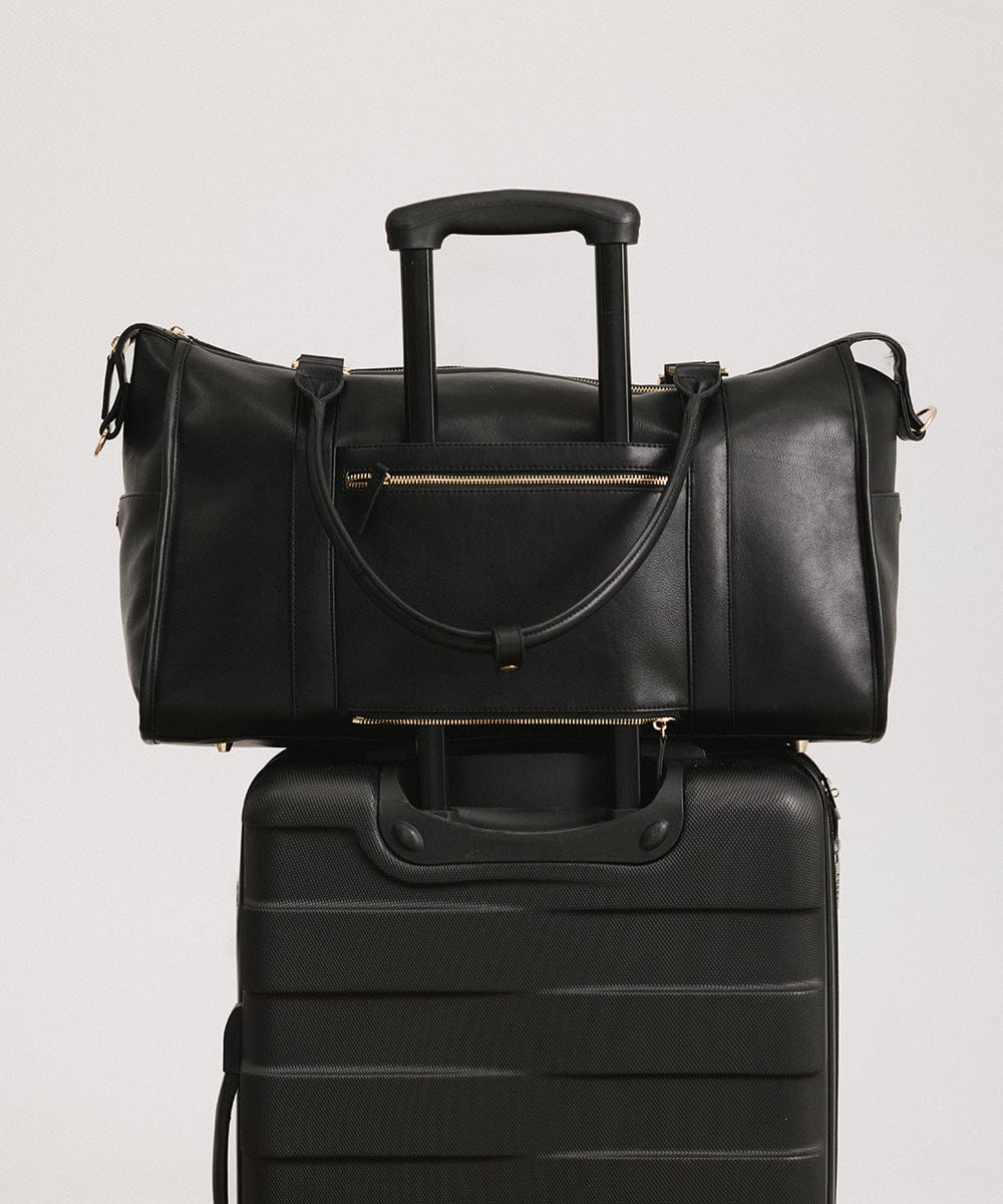 A black vegan leather weekender bag on a black suitcase against a plain background #color_black