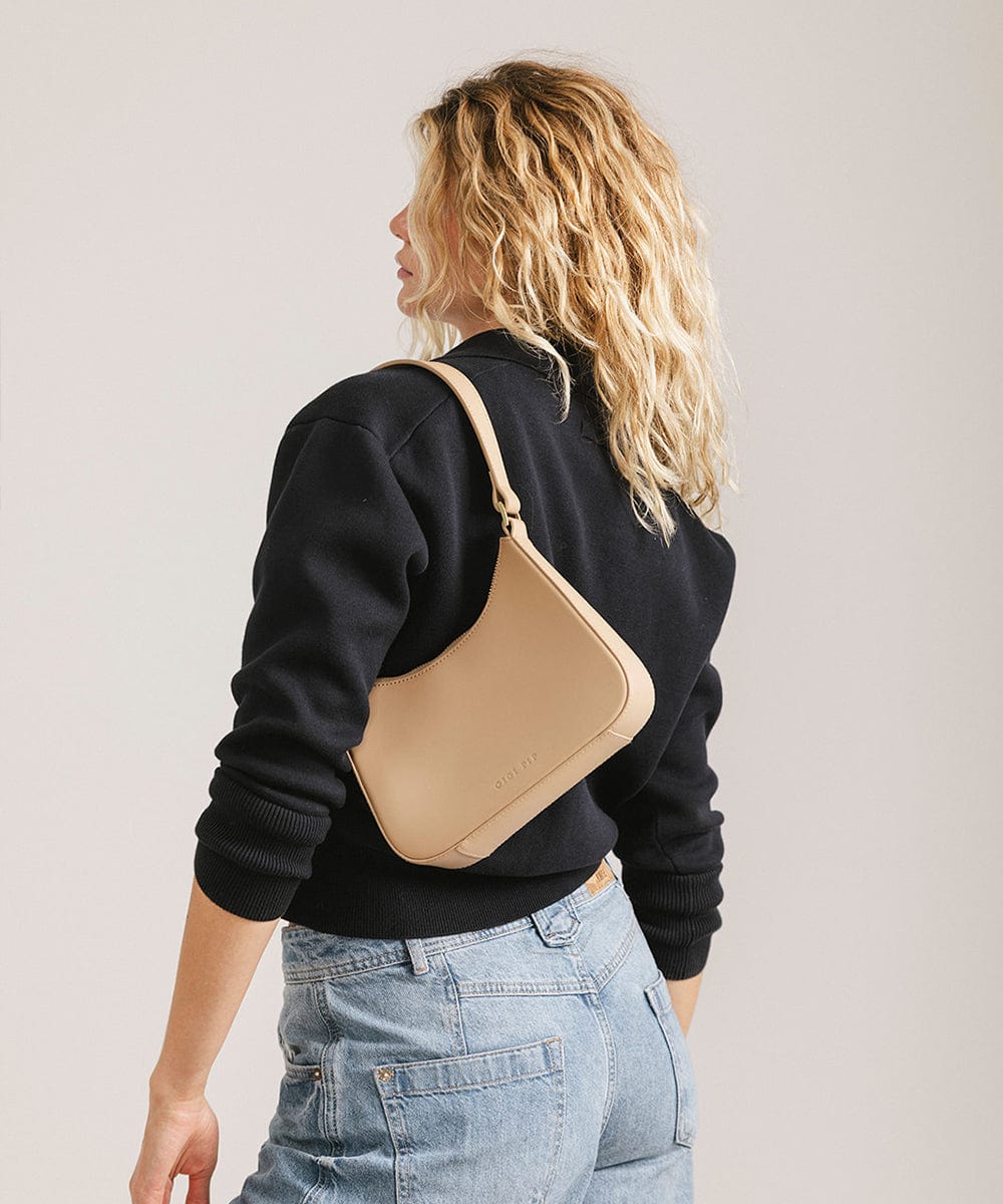 Person wearing a black shirt and denim shorts, carrying a tan genuine leather handbag, facing sideways  against a plain background #color_tan