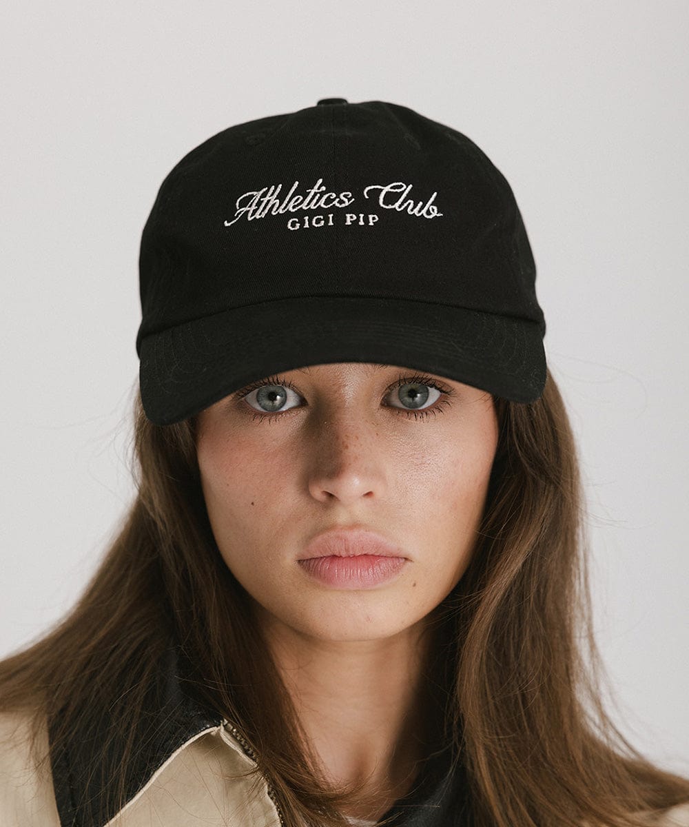 Woman wearing a black cap with white 'Athletics Club' text against a plain background  #color_black