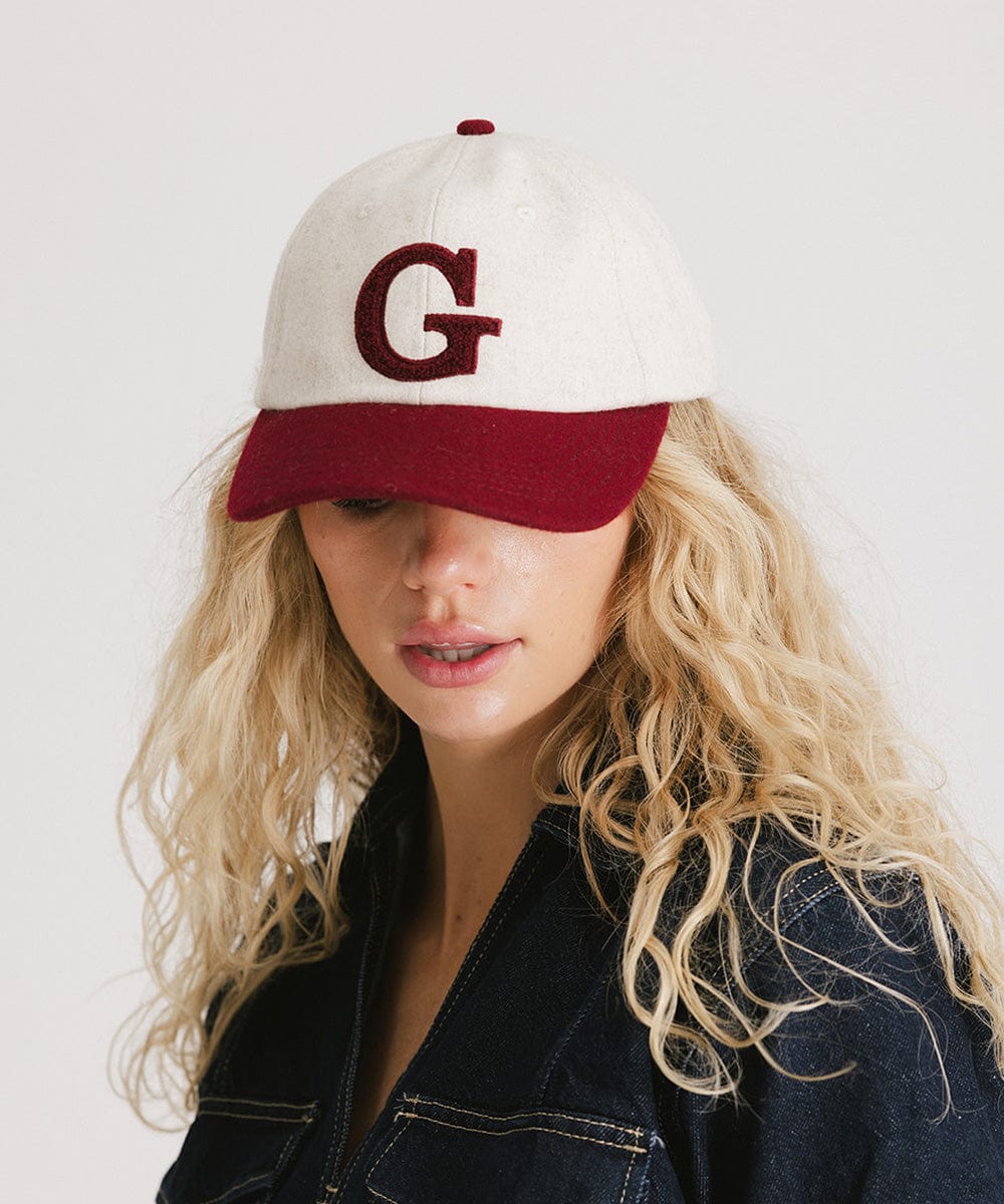 Woman wearing a white and burgundy baseball cap with the letter 'G' and a denim shirt, posing against a plain background  #color_burgundy