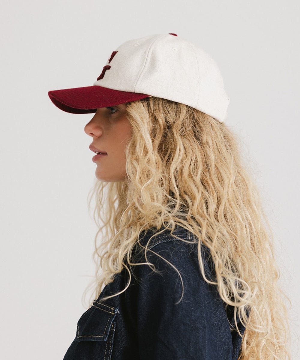 Woman wearing a white and burgundy baseball cap and a denim shirt, facing sideways against a plain background  #color_burgundy