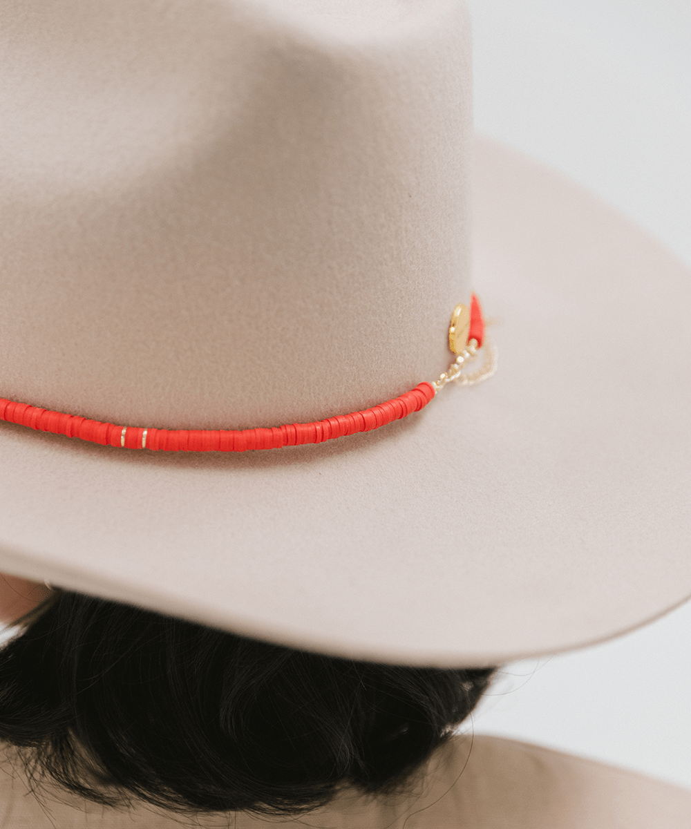A cream hat with a red beaded hat band against a plain background #color_red