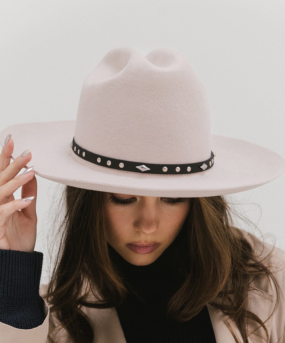 Woman wearing a white hat with a black studded leather hat band against a plain background #color_black