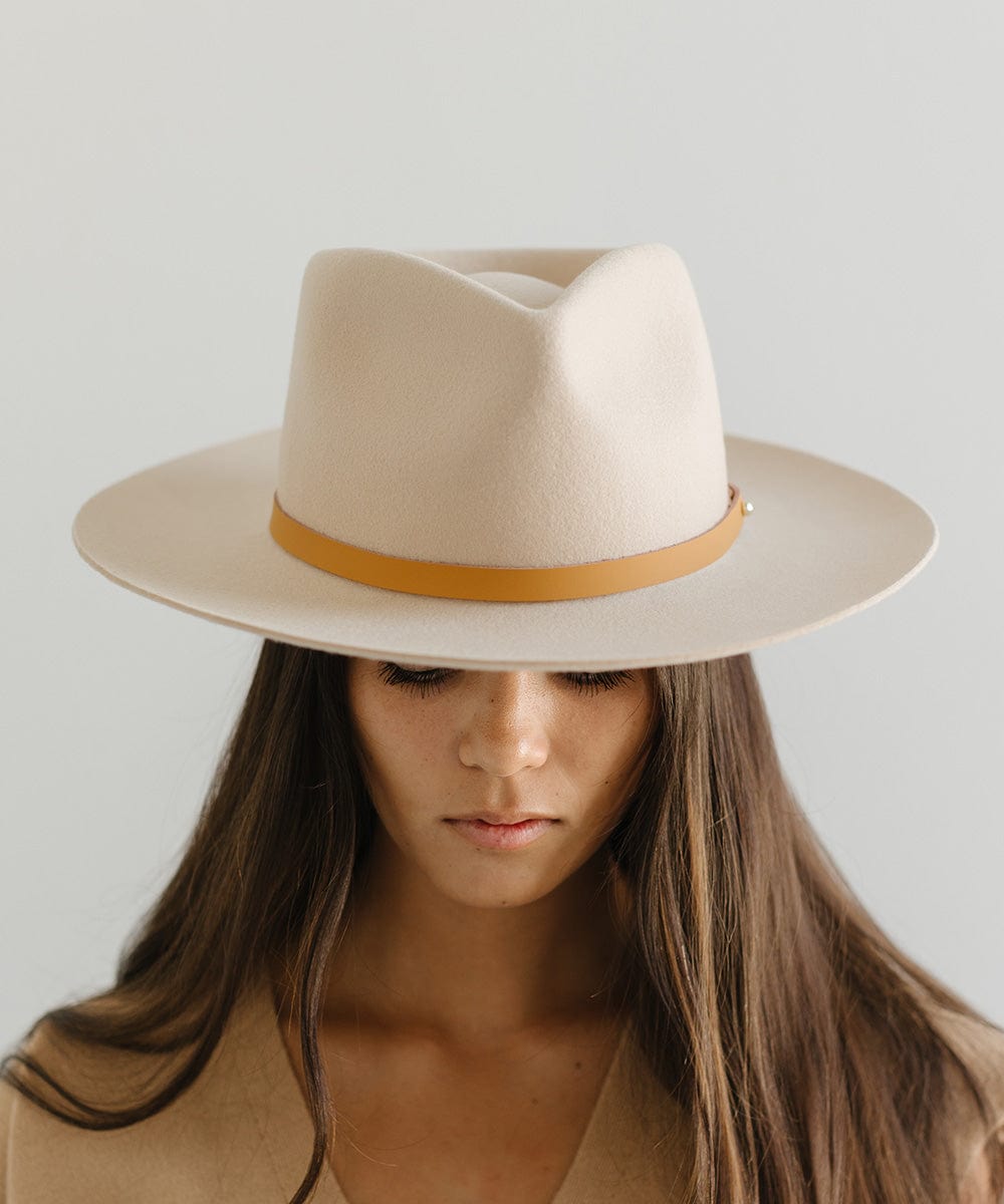 Woman wearing a beige felt hat with a thin camel colored leather hat band around the base against a plain background  #color_camel