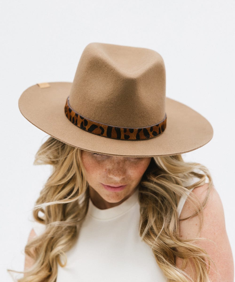 Woman wearing a beige hat with a dark brown leopard print hat band and a white top against a plain background #color_dark brown