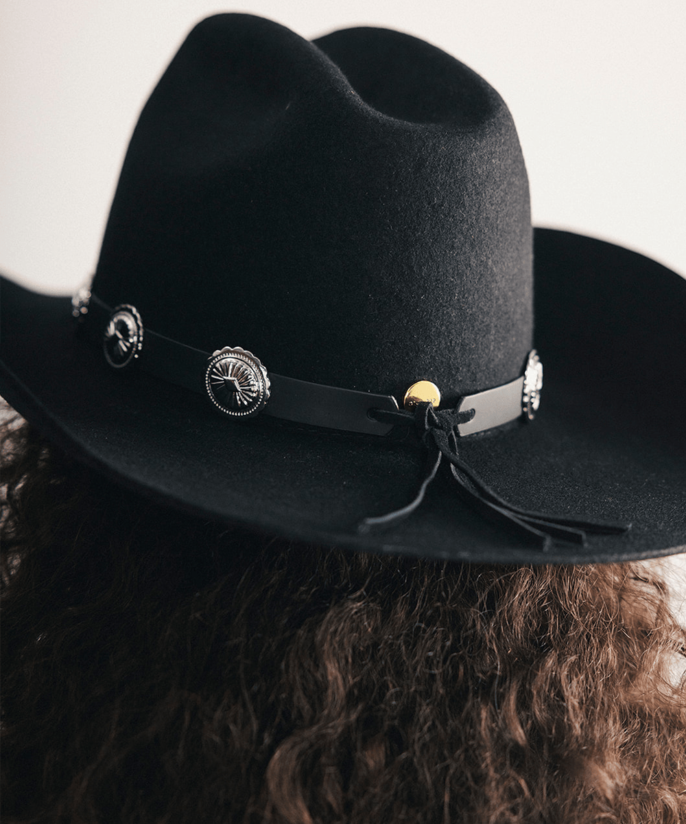 Black cowboy hat with decorative band and conchos on a plain background #color_black