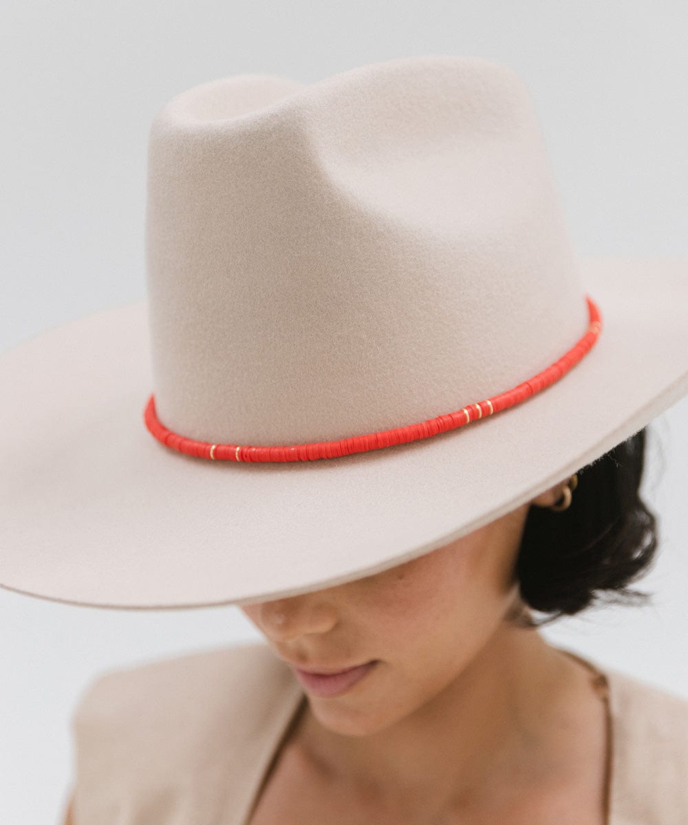 Woman wearing a cream hat with a red beaded hat band against a plain background #color_red