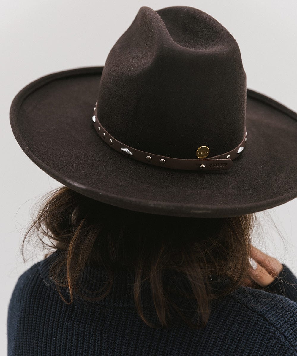 Woman wearing a brown hat with a chocolate colored studded leather hat band against a plain background #color_chocolate