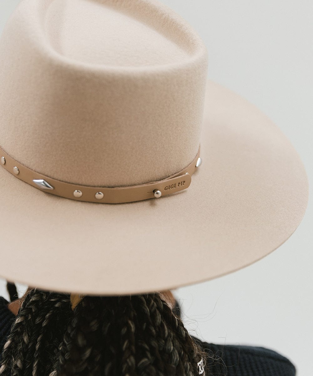Close up image of a person wearing a cream hat with a tan studded leather hat band against a plain background #color_tan