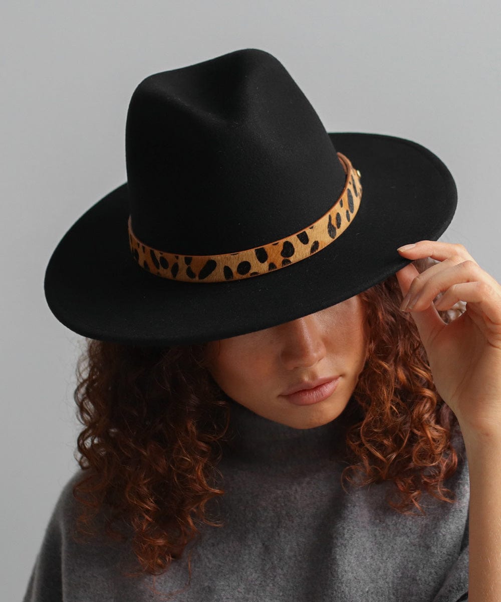 Woman wearing a black hat with a tan leopard print hat band and a grey t-shirt, looking down against a plain background #color_tan